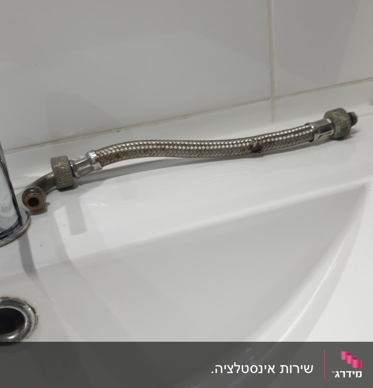 צינור גמיש מתכת ליד כיור לבן